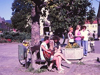 EBI 1990 Sir 051  Pátá etapa čtvrtek 12. 7. 1990 náměstí v Kašperských Horách. V popředí hraje Míra Kratoška (poprvé na Ebicyklu) do ouška jedné z místních koček. Vzadu Milan Antoš, Laděna Vacířová a Mirka Štorková